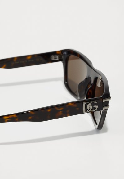 Ochelari de soare din fâșie de țestoasă cu lentile întunecate, având un logo metalic DG pe braț și un design elegant, unghiular al ramei.