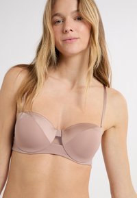 Reggiseno rosa chiaro in tessuto liscio con design a contorno, dotato di sottili spalline regolabili e un dettaglio in rete al centro.
