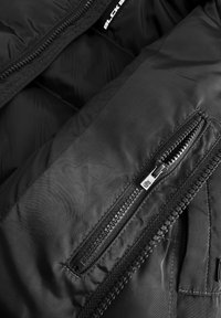 Zwarte geïsoleerde jack binnenkant met een gladde, glanzende nylontextuur. Bevat een ritszak en dikke padding voor warmte.