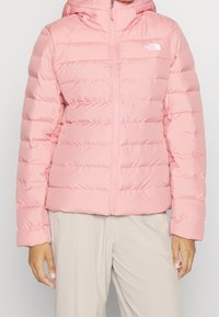 Veste rembourrée rose avec une fermeture éclair à l'avant, design matelassé et capuche. Elle possède des manches longues et une texture douce et lisse.