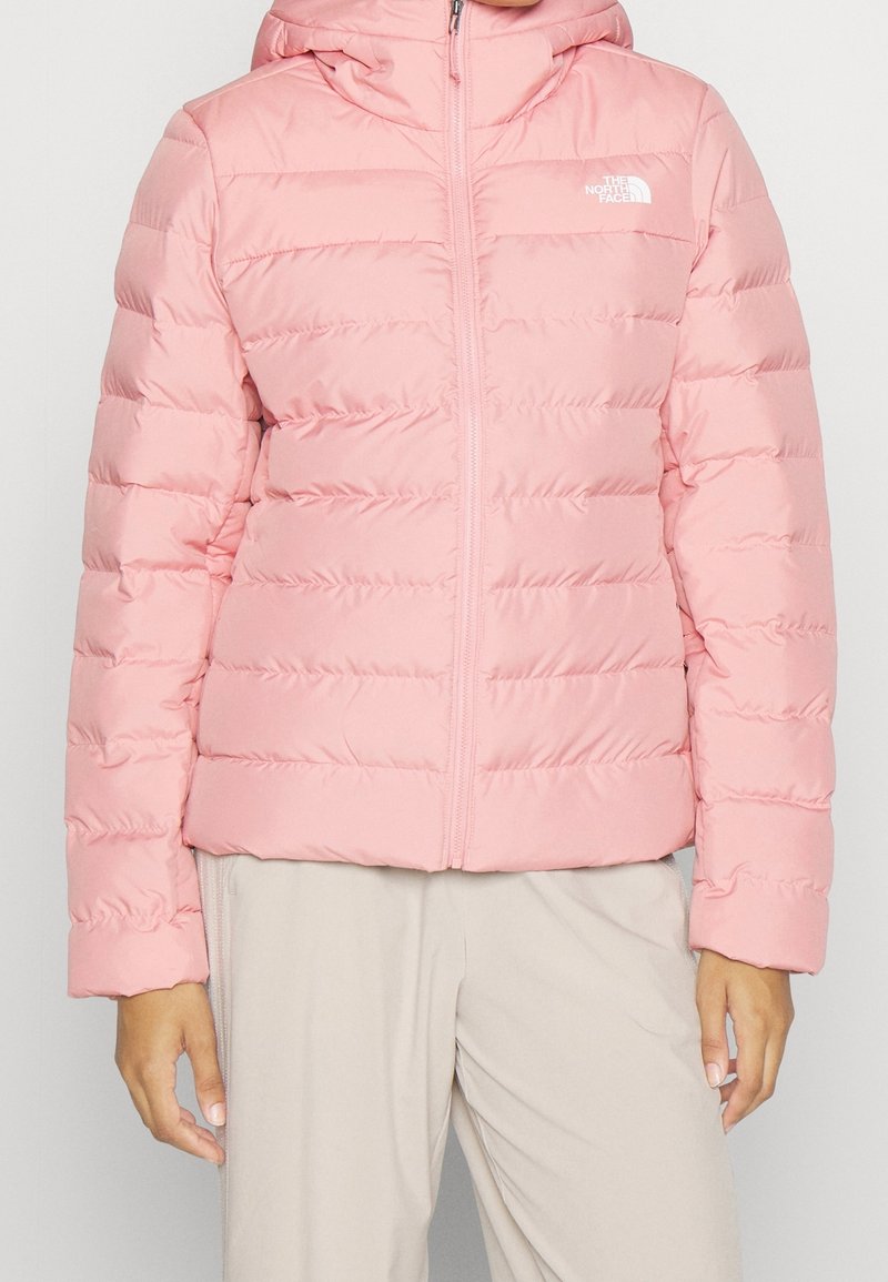 Veste rembourrée rose avec une fermeture éclair à l'avant, design matelassé et capuche. Elle possède des manches longues et une texture douce et lisse.