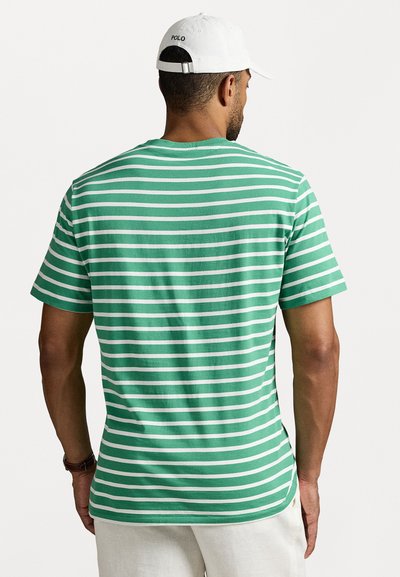 T-shirt în dungi verzi și albe, cu mâneci scurte, din material bumbac, design cu gât rotund, arătând vista din spate cu o margine curbată. Modelul poartă o șapcă albă.