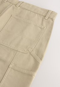 Beige canvas pants featuring a back pocket, belt loops, and double-stitched seams, displaying a smooth texture and structured design.