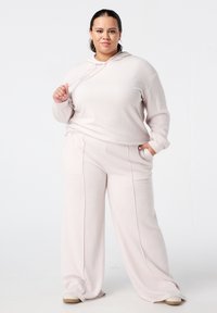 Lichtroze lounge-set met een textuur hoodie met een trekkoord en wijde broekspijpen. Beide stukken hebben zijzakken.