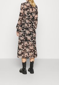 Czarna sukienka w kwiaty do połowy łydki z długimi bufiastymi rękawami, ozdobiona różowymi i beżowymi kwiatami, stylizowana z czarnymi botkami za kostkę.