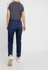 Jeans in denim blu scuro con una vestibilità slim, dotati di tasche posteriori e di una patta in pelle marrone. La parte superiore presenta un motivo a righe con dettagli in pizzo.