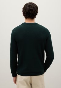 Maglione lavorato a maglia verde scuro con scollatura rotonda e maniche lunghe, caratterizzato da un design testurizzato. Polsini e orlo a coste.