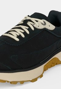 Baskets noires et beiges avec lacets blancs, semelle beige épaisse et bande de roulement jaune, gros plan sur les détails avant et côté.