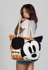 Bolsa de mano de lona con una gran cara de Mickey Mouse en blanco y negro, con acentos en naranja y blanco y asas de cuerda natural.