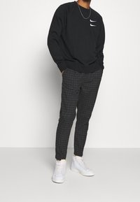 Svart sweatshirt med två vita Nike-logotyper på bröstet, ihop med grå rutiga byxor och vita sneakers.
