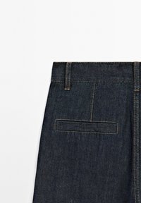 Tmavé denimové džíny se střih na rovno, obsahující zadní kapsu obdélníkového tvaru, viditelné švy a středně vysoký pas.