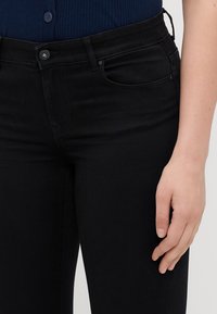 Melnas denima bikses ar pieguļošu dizainu, ar pogu un rāvējslēdzēju, priekšējo kabatu un nelielu izstieptu tekstūru.