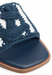 Sandal in tessuto blu navy con una fascia testurizzata decorata da un motivo geometrico bianco, completata da una suola scura e liscia e suola marrone.