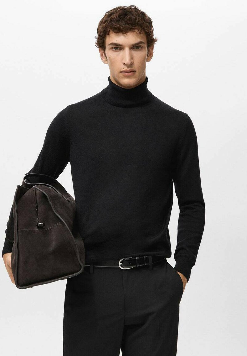 Zwarte coltrui van fijngebreid materiaal, gecombineerd met donkere broek. De persoon houdt een bruine suède tas met rits vast.