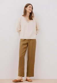 Beige V-hals top met kantdetails, gecombineerd met bruine wijde broek en bruine sandalen met bandjes. Eenvoudig, ontspannen ontwerp.