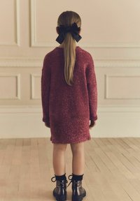 Robe pull sparkly bordeaux à manches longues, associée à des bottes noires à lacets et un nœud noir dans les cheveux, vue de dos.