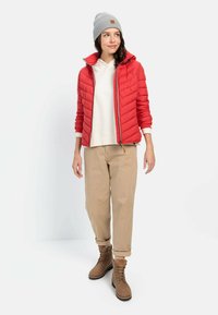Rød quiltet pufferjakke, grå strikket hue, off-white hoodie, tan bukser og brune snørebukser. Har strukturerede materialer og praktisk design.