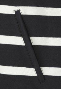 Tissu rayé noir et blanc avec une finition texturée, comportant une poche fendue étroite sur le côté, soulignée par une couture contrastante.