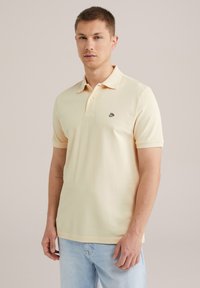 Polo krekls maigi dzeltenā kokvilnā, ar salocītu apkakli, �īsām piedurknēm, trīs pogu aizdari un mazu melnu logo uz krūtīm.