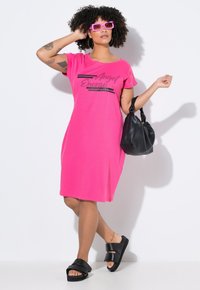 Rosa bomullsklänning med korta ärmar och lös passform, med en tryckt design. Svarta sandaler med breda remmar och en slapp svart väska.