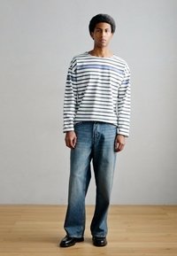 Μπλούζα με μακριά μανίκια και ρίγες σε λευκό και ναυτικό μπλε, σε συνδυασμό με ανοιχτόχρωμο μπλε τζιν. Η μπλούζα έχει άνετη γραμμή, και το τζιν είναι σε φαρδιά κοπή.