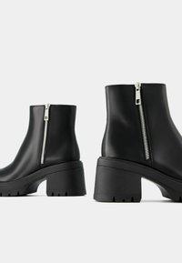 Bottines noires en matériau lisse, dotées d'une fermeture éclair latérale, d'une plateforme épaisse et d'une semelle en caoutchouc texturée pour une bonne adhérence.