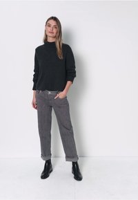 Grijze gebreide trui met hoge hals, gecombineerd met grijze broek met omgeslagen boorden en textuur. Draagt zwarte leren enkellaarsjes. Eenvoudig, modern ontwerp.