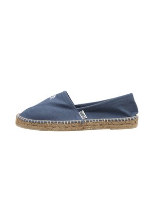 Espadrille en tissu bleu marine avec semelle en jute tissée, style slip-on, et petite étiquette logo blanche sur le côté.