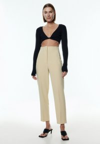Zwarte geribbelde crop top, beige hoog-Waisted broeken, strakke pasvorm. Zwarte haksandalen met brede banden. Schone, minimalistische uitstraling.