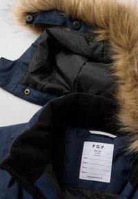 Mørkeblå jakke med en faux fur hætte. Sort inderside. Etiketten på kraven angiver størrelse 116 og plejeanvisninger.