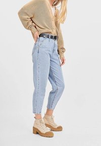 Jasno beżowy sweter z dzianiny zapinany na guziki, noszony na białej koszulce. Spodnie dżinsowe w jasnoniebieskim kolorze z wysokim stanem oraz kremowe botki za kostkę z grubą podeszwą.