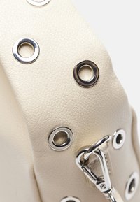 Cream-colored leather bag featuring silver grommets, a textured surface, and a metallic clip for closure.