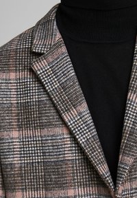 Rutigt kavaj med bruna, grå och rosa toner; strukturerad tyg; spetsig slag; bärs över en svart turtleneck, som visar lagrade designer.