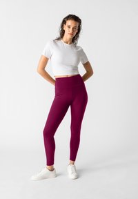 Hoog taille burgundy leggings gemaakt van rekbaar materiaal, gecombineerd met een getailleerd wit T-shirt en witte sportschoenen. Over het geheel een gladde textuur.