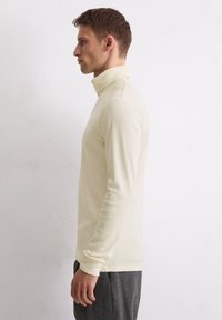 Cremfarbener langärmeliger Rollkragenpullover aus weichem Stoff, taillierte Passform mit gerippten Bündchen, glatte Textur und minimalistischer Stil.