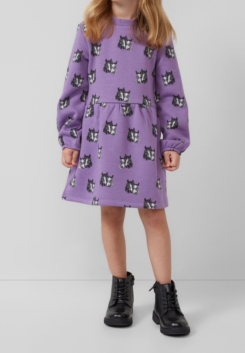 Enfant portant une robe à manches longues violette imprimée de visages de chiens noirs et blancs, associée à des bottes noires à lacets.