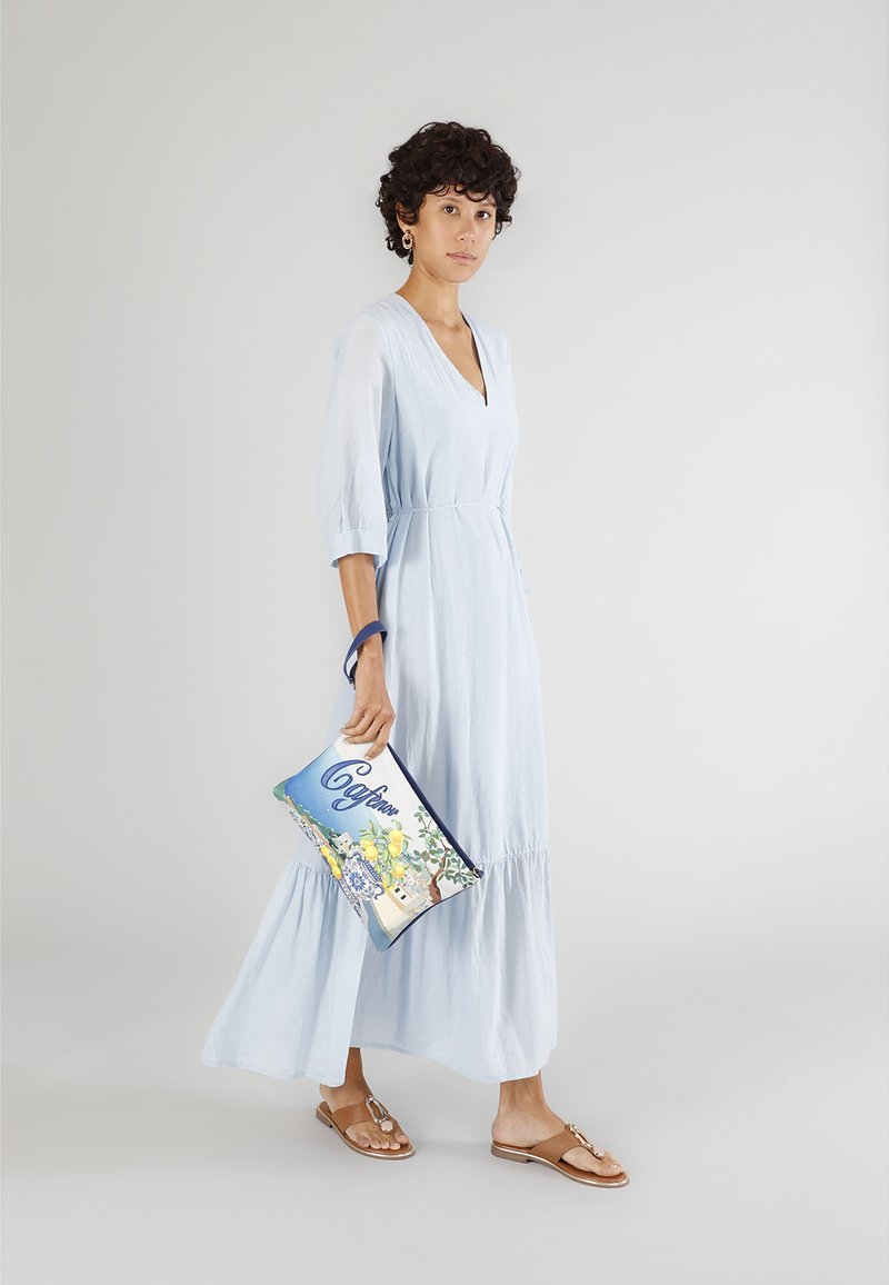 Ljusblå, långärmad klänning med en rynkad kjol, bärs med bruna sandaler. Håller en färgglad handväska med blommönster.