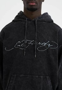 Black hoodie made of soft fabric featuring a large, stitched logo in dark gray and a front pocket. Includes drawstrings with silver tips.