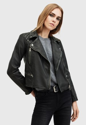 Giacca da biker in pelle nera con spalle trapuntate, dotata di zip argentate e taglio slim. Indossata sopra un maglione grigio con jeans neri.