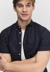 Kortärmad marinblå knapp-up skjorta, i bomullstyg, skräddarsydd passform, med vita knappar. Modellen bär en vit t-shirt under.