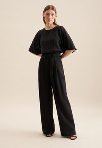 Set coordinato nero composto da una maglietta a maniche corte con vestibilità ampia e pantaloni a gamba larga. Realizzato in un tessuto testurizzato con una finitura opaca.