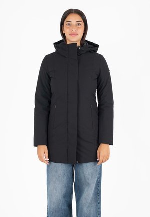 Zwarte lange jas met capuchon, gemaakt van textuurstof. Heeft een ritssluiting aan de voorkant, zijzakken en een licht taps toelopende snit. Kleding gedragen over losse jeans.