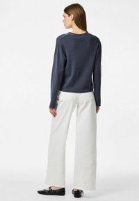 Jersey de punto azul marino con un corte relajado, combinado con pantalones anchos blancos y zapatos planos negros, visto desde la espalda.