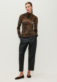 Brown patterned long-sleeve top with a high neck, paired with black faux leather trousers and brown suede flats. Textured fabric detail visible.