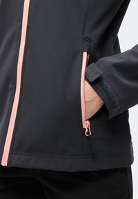 Veste noire avec fermeture éclair rose et poignet en velcro, montrant une main à l’intérieur de la poche latérale zippée.