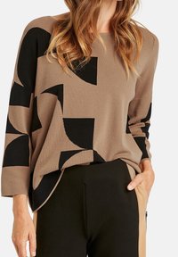 Brown and black patterned sweater with a loose fit and long sleeves. Soft knit fabric with geometric designs. Paired with black pants.