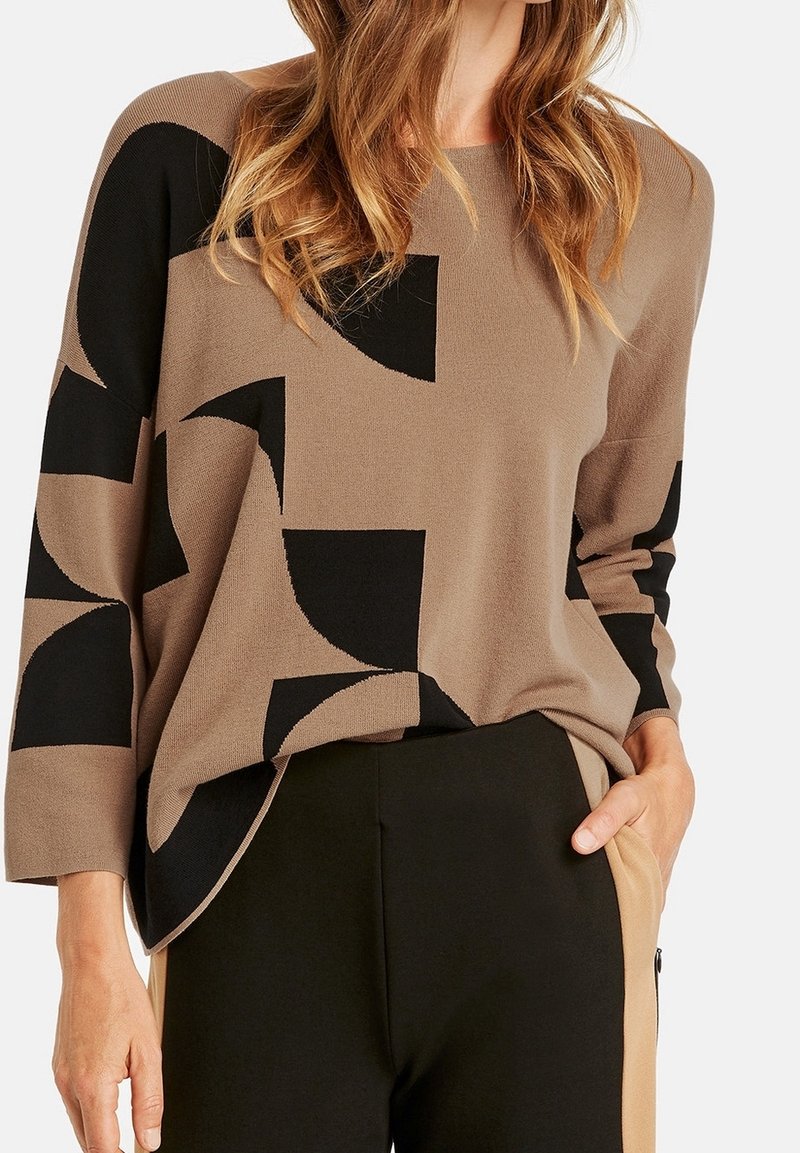 Brown and black patterned sweater with a loose fit and long sleeves. Soft knit fabric with geometric designs. Paired with black pants.