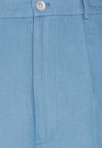 Ljusblått linne tyg med en subtil vävstruktur. Har en framknappstängning och en ficka. Ren, skräddarsydd design.