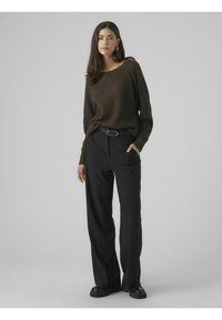 Mørkegrøn waffle-strikket sweater med en bred halsudskæring, parret med sorte højtaljede bukser med lommer og et bælte med en sølvspænde.