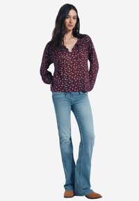 Blusa floreale marrone con scollatura a V e cordoncino. Maniche lunghe e tessuto leggero abbinato a jeans a palazzo azzurri chiari. Calzature beige.